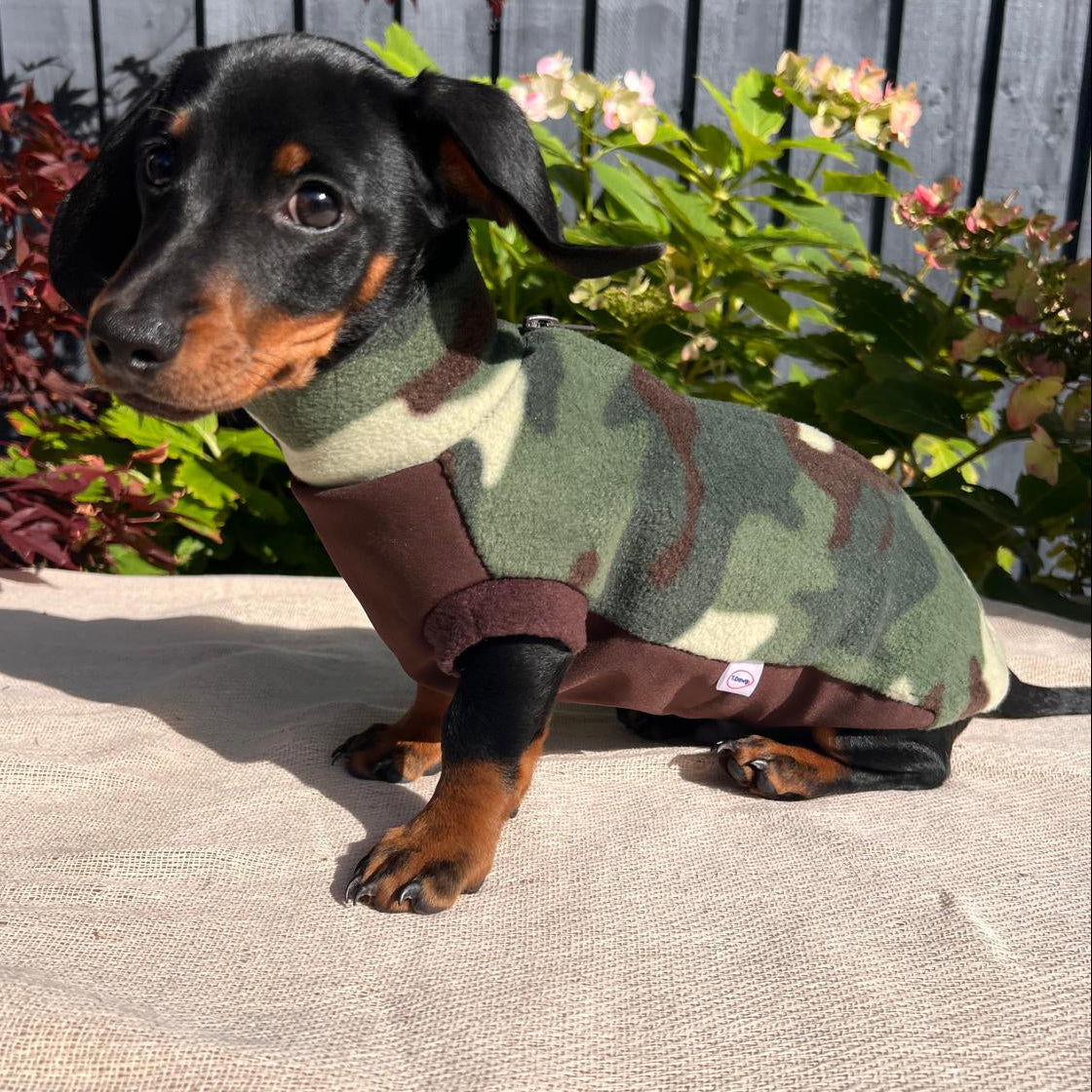 Dog wearing a camouflage sweater sitting outdoors on a patio.
